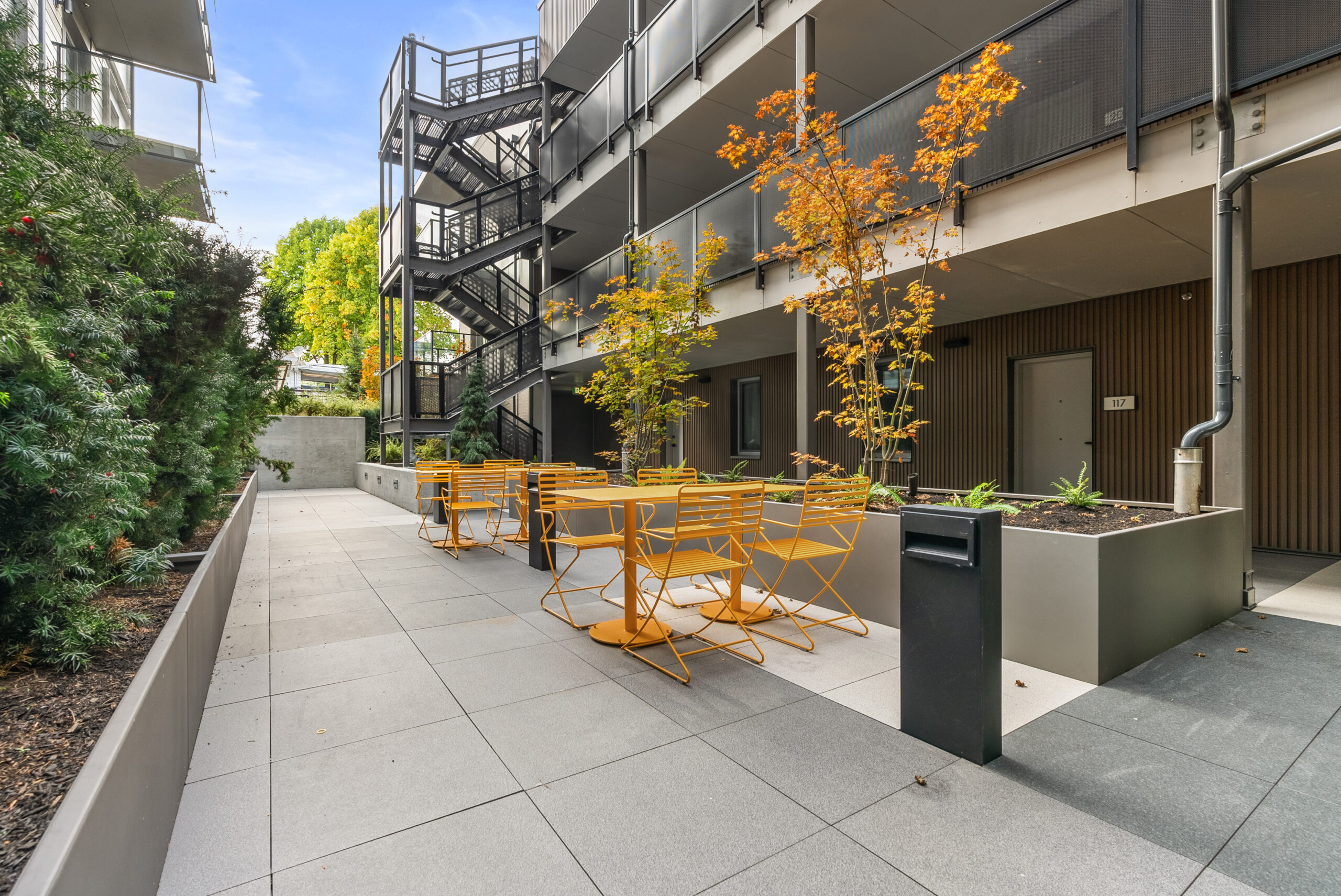 Outdoor seating area at McHardy apartment building in Vancouver with yellow chairs, planters, and stair access.