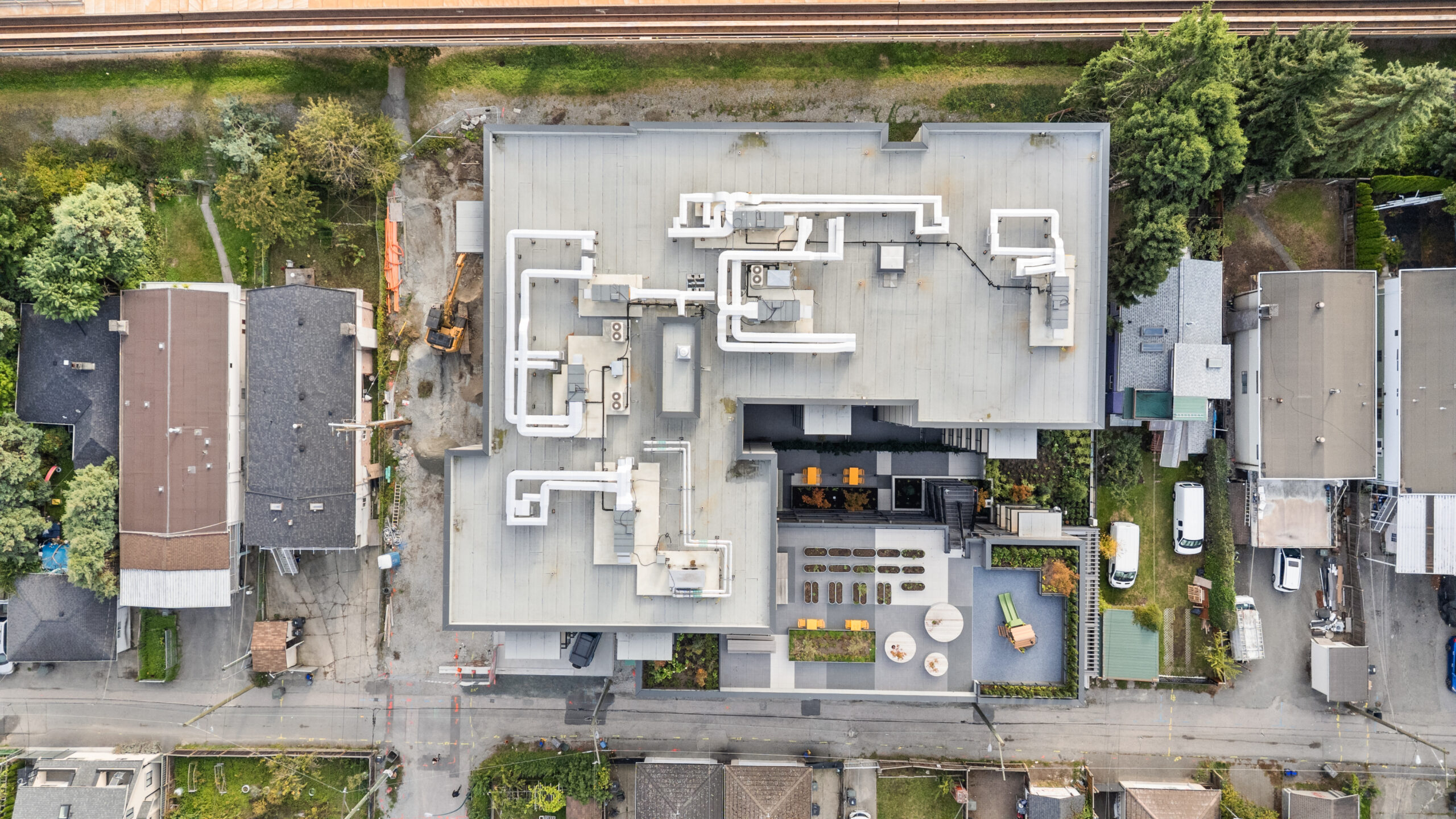 Aerial view of McHardy apartment building in Vancouver with flat roof, HVAC structures, and rooftop patio areas, surrounded by houses.