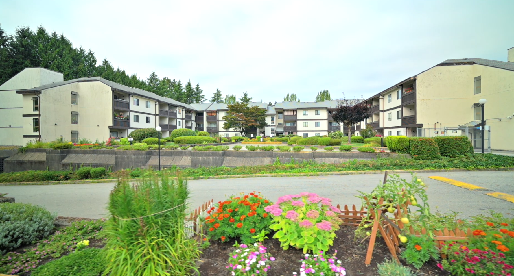 Front view of Packard Housing Co-op in Coquitlam with landscaped greenery and colorful flower garden in the foreground.