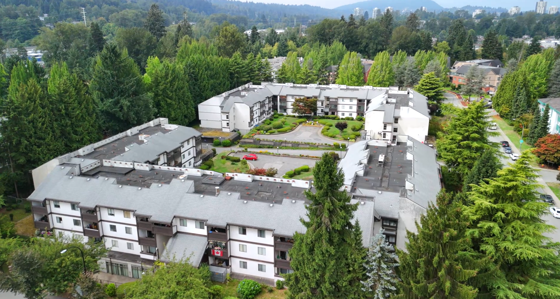 Aerial view of Packard Housing Co-op in Coquitlam, showing U-shaped layout, landscaped courtyard, and surrounding trees.