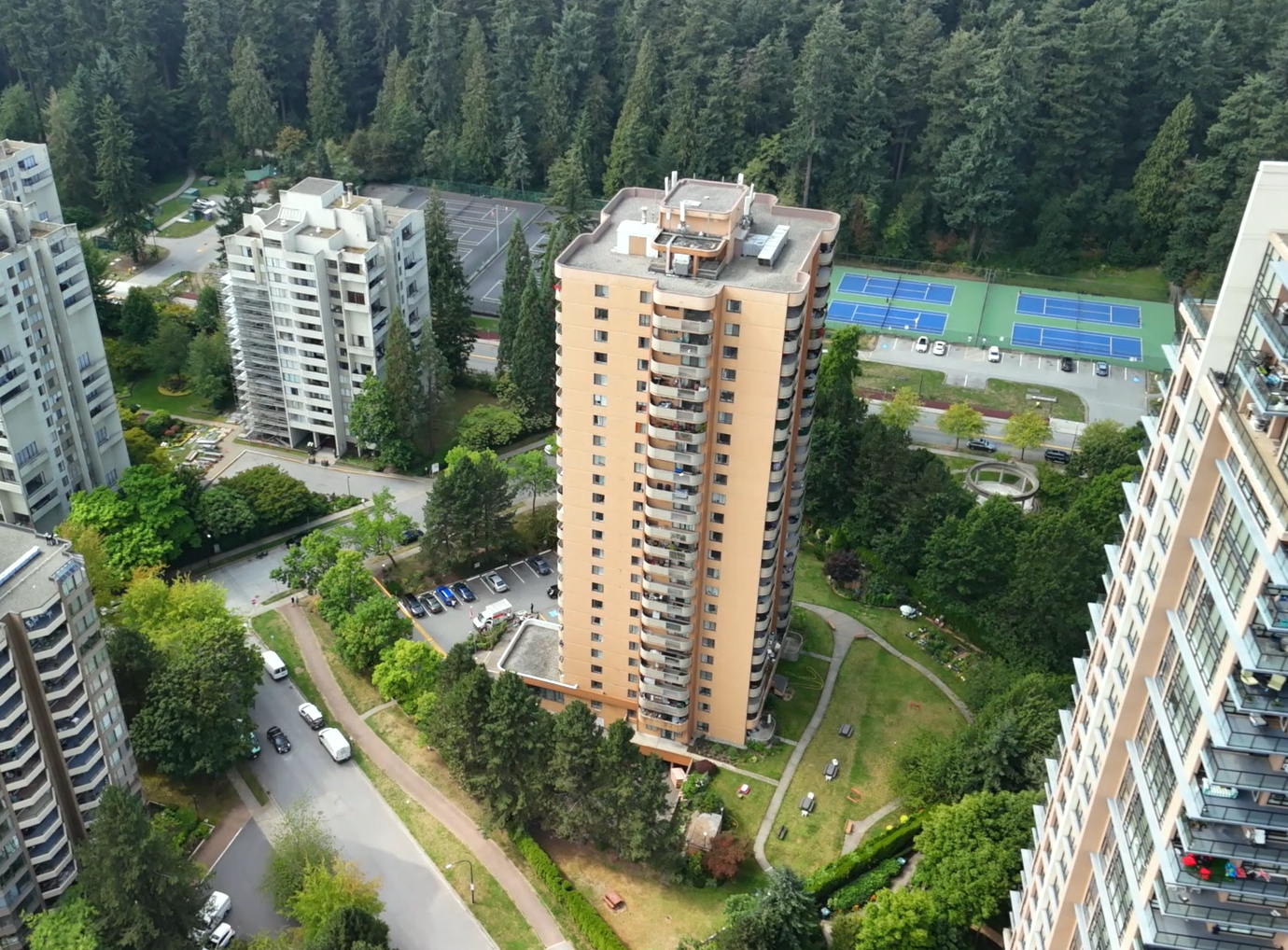 Aerial view of Post 83 Housing Co-op in Coquitlam with tall residential tower, green spaces, and nearby tennis courts.”
