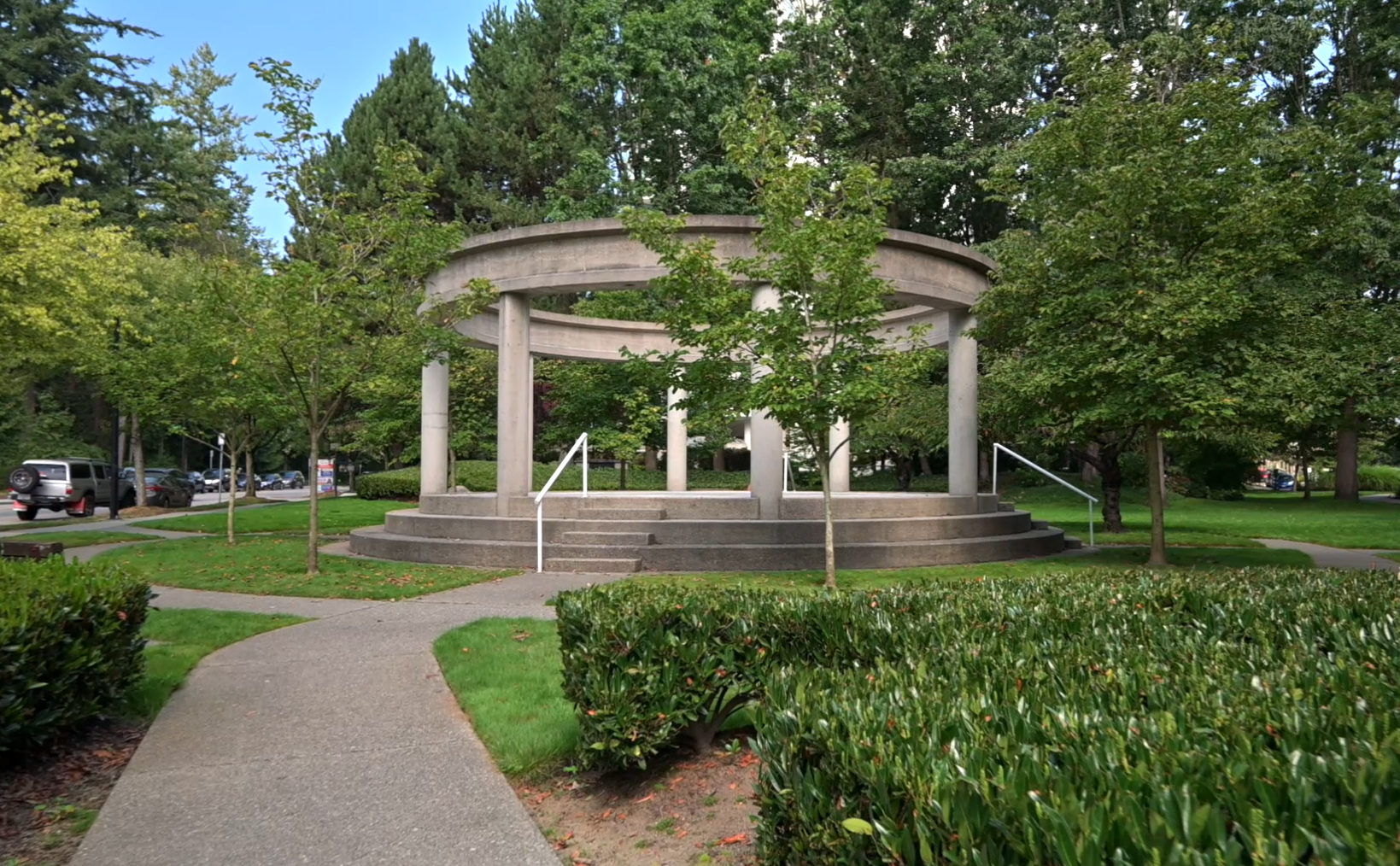 Circular concrete pavilion surrounded by green trees and manicured shrubs at Post 83 Housing Co-op in Burnaby.