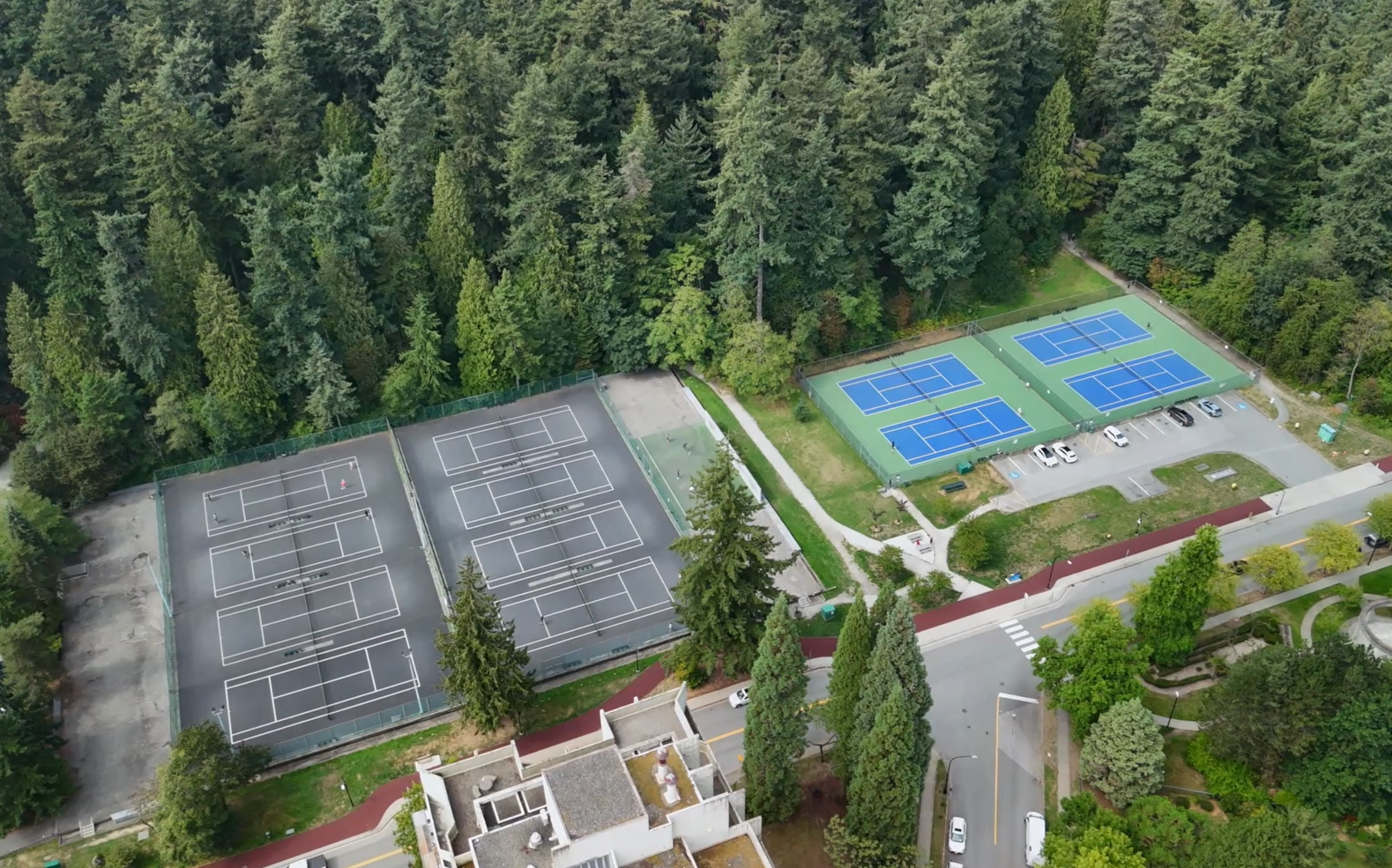 Aerial view of tennis courts near Post 83 Housing Co-op in Burnaby, surrounded by tall evergreen trees.